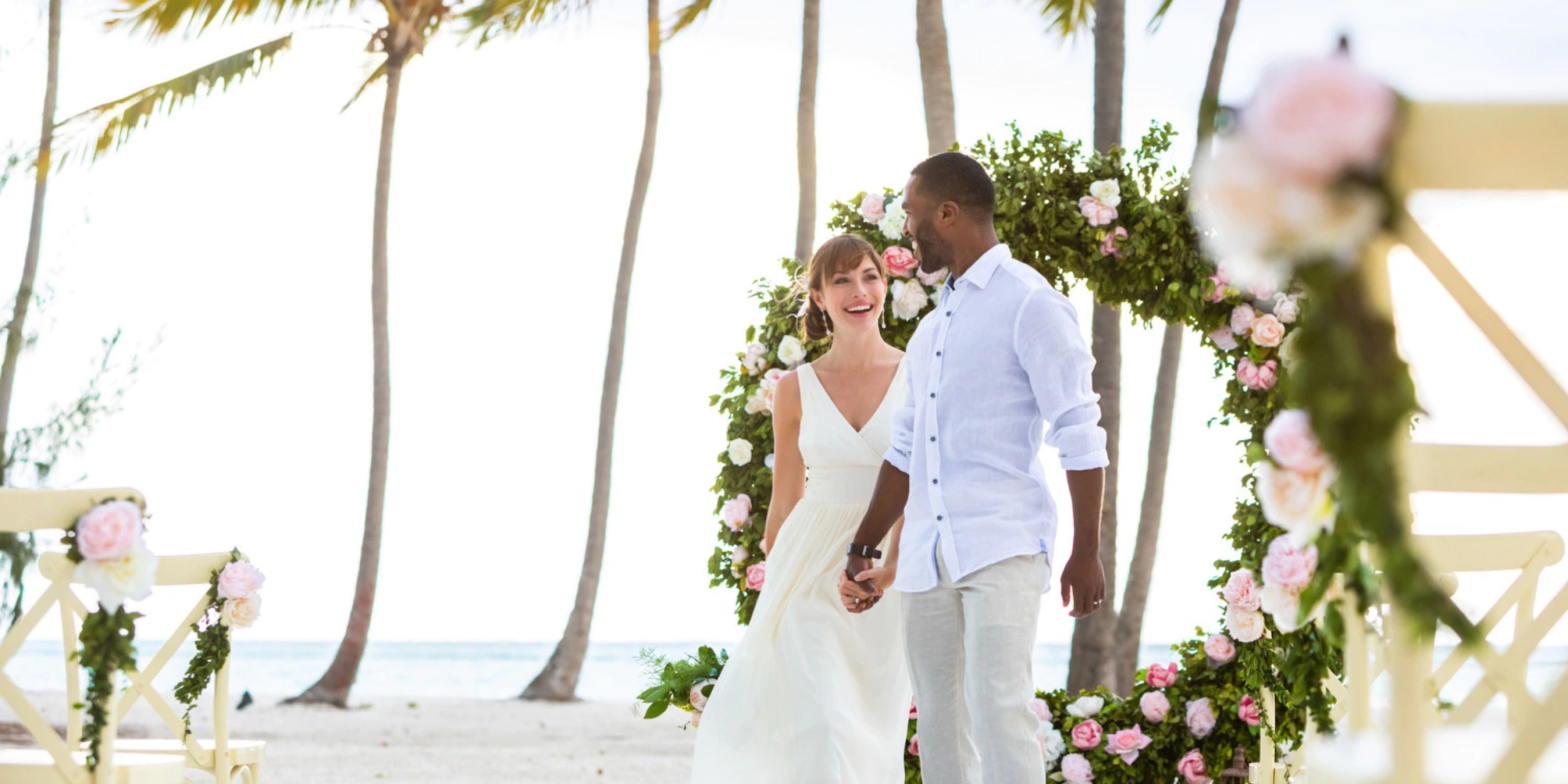 Newlywed couple walking beneath a floral arch on the beach at Hyatt Zilara Cap Cana after their wedding ceremony.